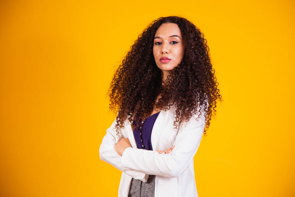 Joven mujer de negocios afro con los brazos cruzados sobre fondo amarillo. - Foto, Imagen