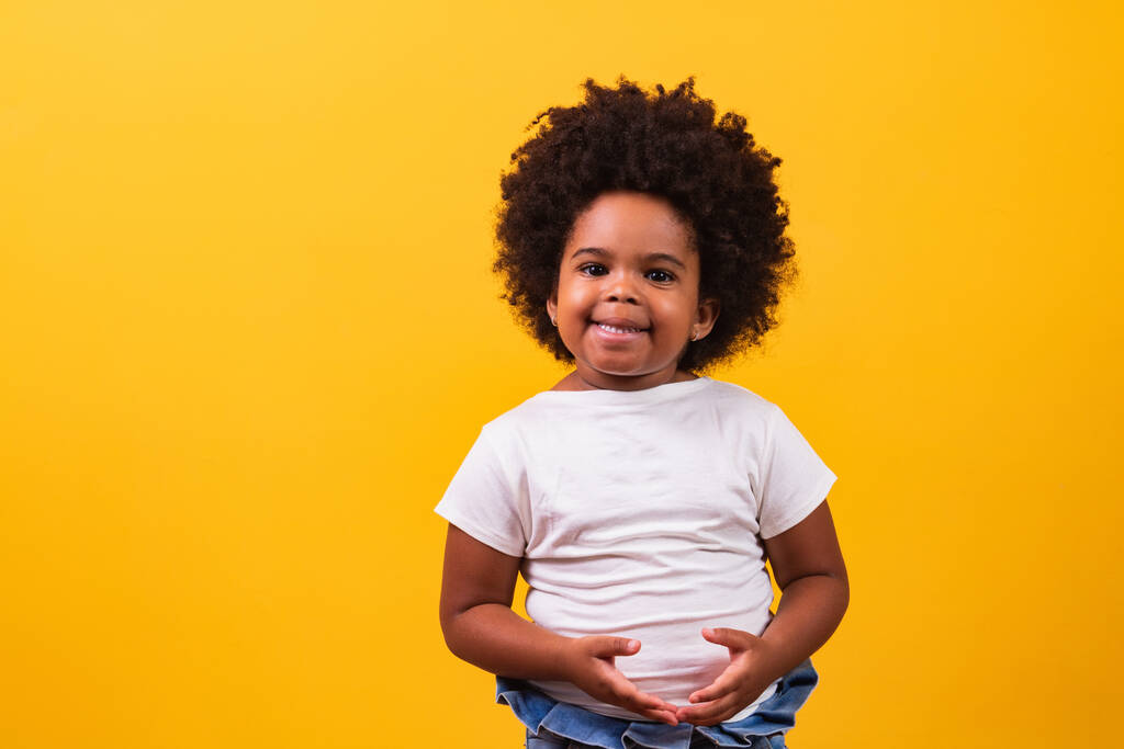 Koncepcja dzieciństwa i ludzi - szczęśliwa, mała afrykańska dziewczyna na żółtym tle. Mała czarna dziewczyna z czarnymi włosami mocy uśmiechnięta. - Zdjęcie, obraz