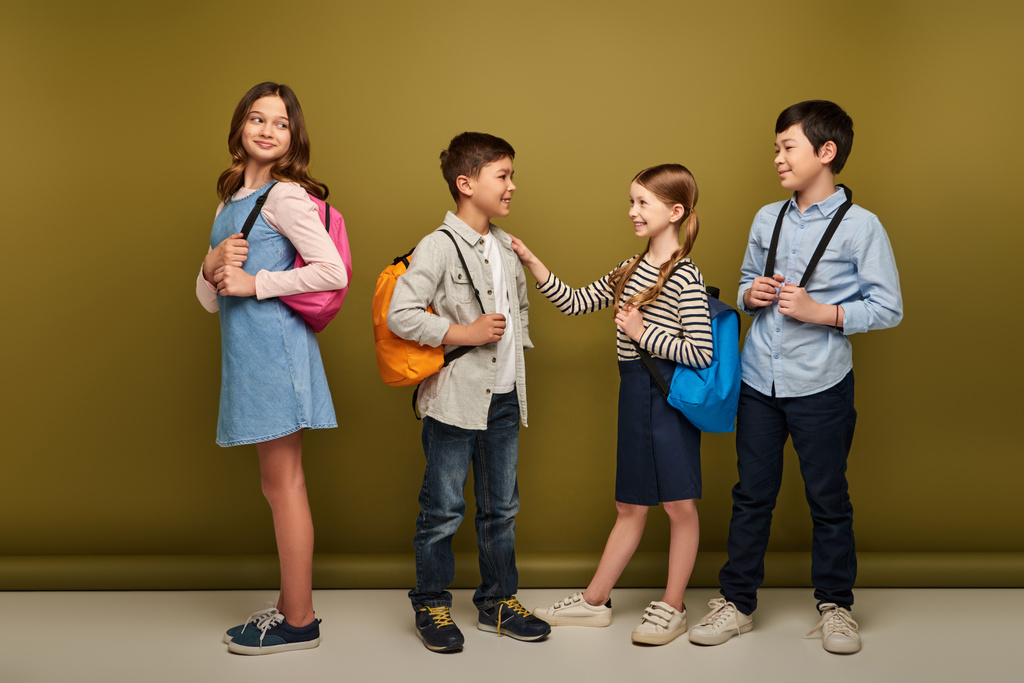 Повна тривалість усміхнених міжрасових дітей з рюкзаками, які дивляться на друзів, які розмовляють під час міжнародного святкування дня захисту дітей на фоні хакі
 - Фото, зображення