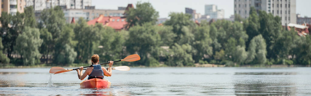 powrót widok aktywnych wielonarodowych przyjaciół w kamizelkach ratunkowych pływających sportowym kajakiem z wiosłami na rzece miejskiej z zielonym brzegiem podczas weekendu rekreacyjnego w lecie, sztandar - Zdjęcie, obraz