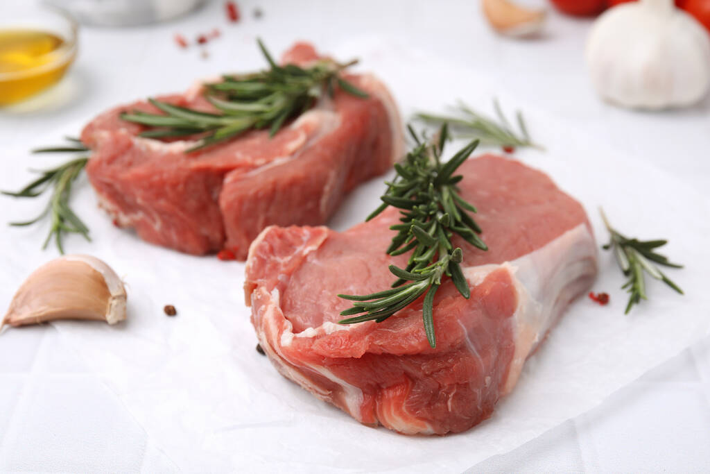 Carne fresca cruda con romero sobre mesa blanca, primer plano - Foto, Imagen