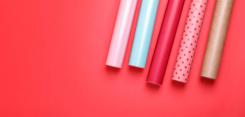 Rolos de papéis de embalagem coloridos em fundo vermelho, flat lay. Espaço para texto - Foto, Imagem