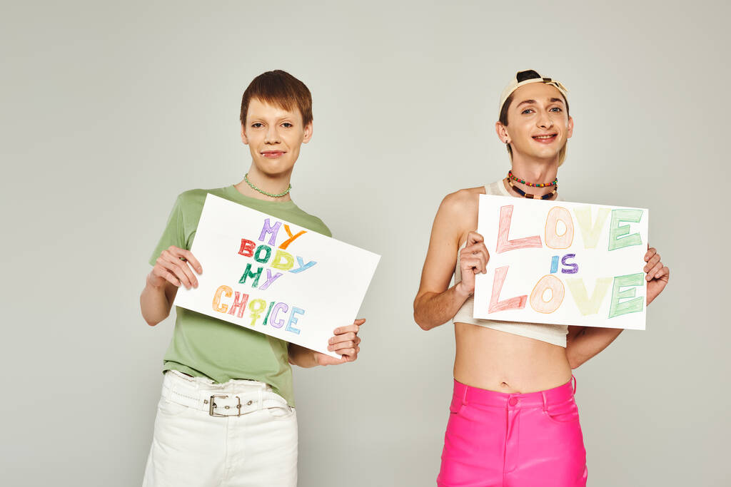 gelukkig gay mannen holding plakkaten met mijn lichaam mijn keuze en liefde is liefde belettering terwijl staan samen en kijken naar camera op trots maand grijs achtergrond  - Foto, afbeelding