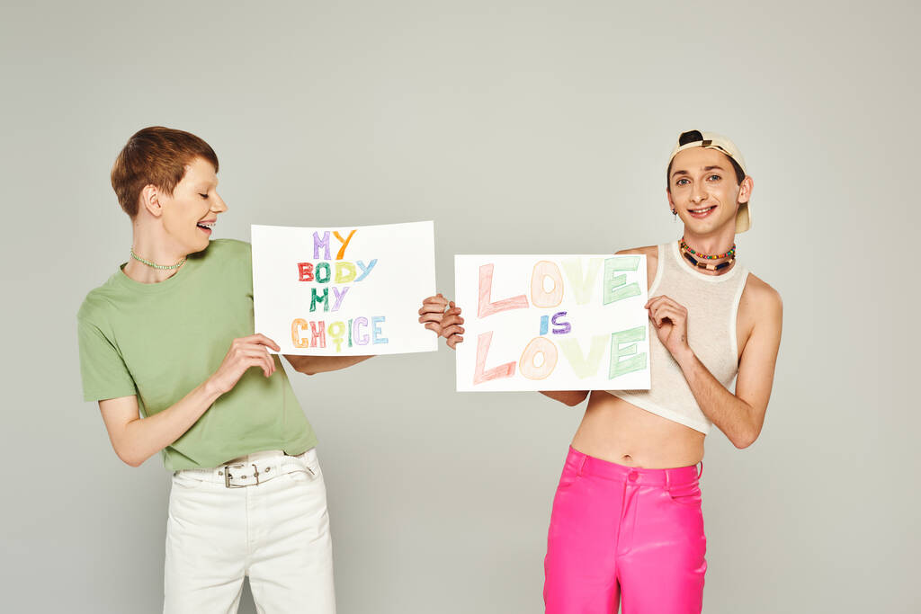 happy lgbt friends holding placards with love is love and my body my choice lettering while standing together on pride month, grey background  - Photo, Image
