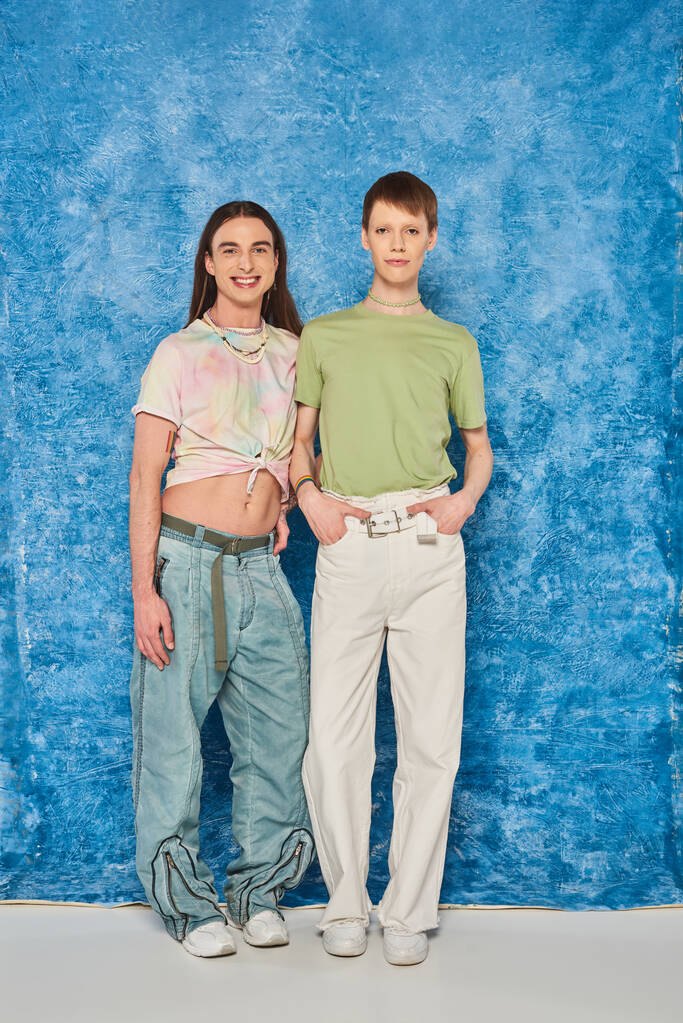 pełna długość uśmiechnięty gej przyjaciele w casual ubrania pozowanie i patrząc w aparat podczas świętowanie lgbt duma miesiąc na mottled niebieski tło - Zdjęcie, obraz