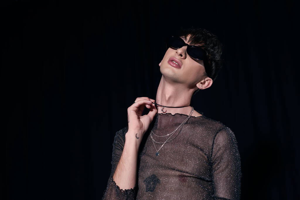Модный гей в солнцезащитных очках и блестящий топ трогательное ожерелье во время lgbt сообщества и праздник месяц гордости изолированы на черном  - Фото, изображение