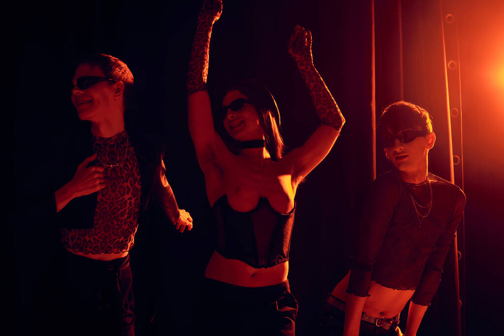 Innoissaan ryhmä homo ystäviä aurinkolasit ja tyylikkäät vaatteet tanssia juhlien aikana ja lgbt ylpeys kuukausi juhla mustalla taustalla punaisella valolla  - Valokuva, kuva