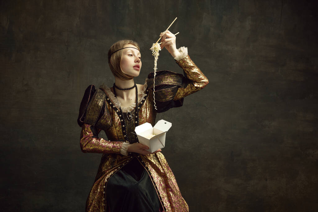 Portrét mladé dívky, královská osoba, princezna ve vinobraní šaty jíst nudle s hůlkami na tmavozeleném pozadí. Koncept historie, remake renesančního umění, srovnání éry - Fotografie, Obrázek