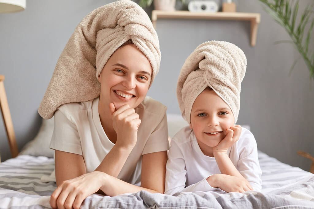 Portrait de beauté de maman et fille heureuses en serviettes sur la tête allongées sur le lit à la maison, posant après le bain, ayant une journée spa, mignonne petite fille et sa mère s'amusent ensemble. - Photo, image