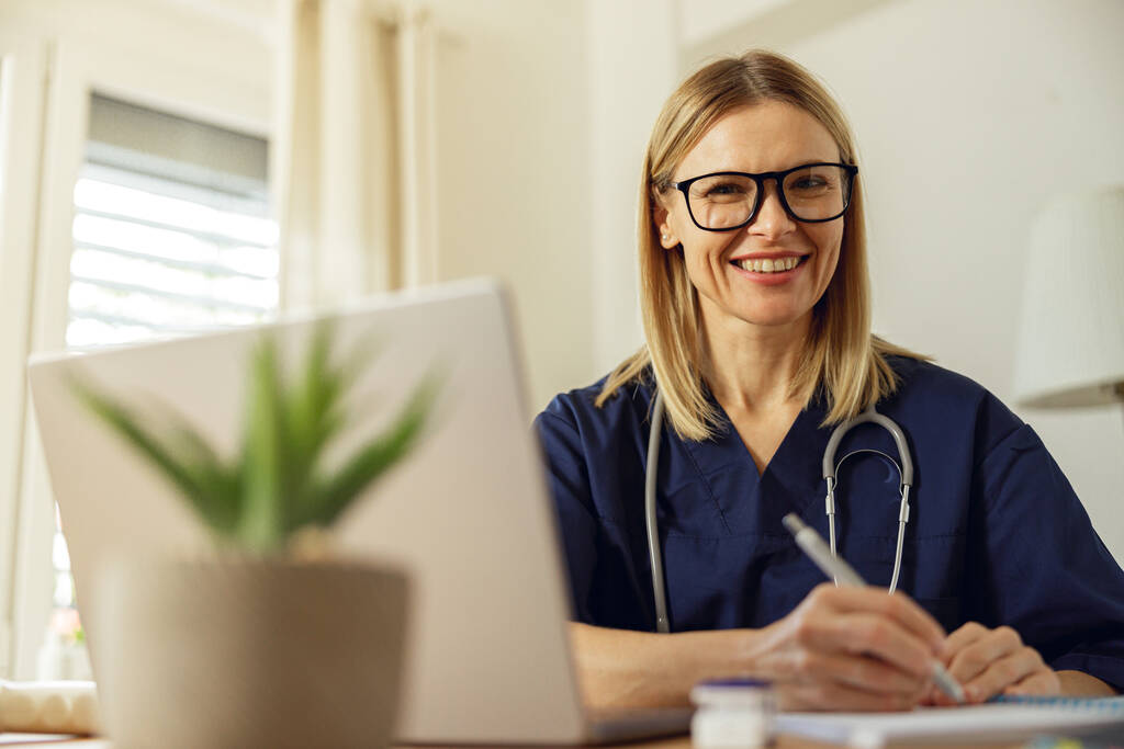 女性医療従事者が書類作成やノートパソコンの使用をしながら、医師事務所で働く笑顔 - 写真・画像