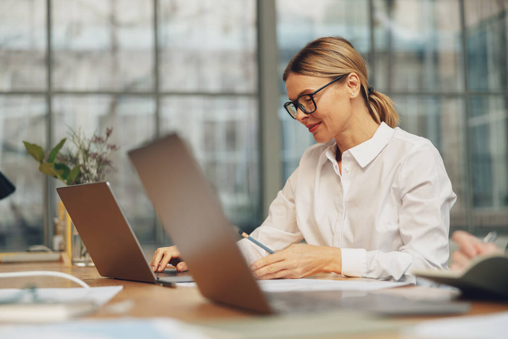 Csinos női irodai dolgozó dolgozik laptop, miközben ül a modern coworking. Kiváló minőségű fénykép - Fotó, kép