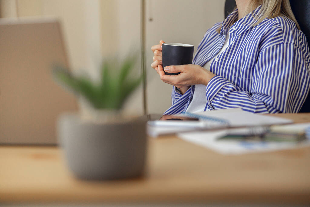 Улыбающаяся женщина пьет кофе во время перерыва, работая из дома. Концепция работы на расстоянии - Фото, изображение