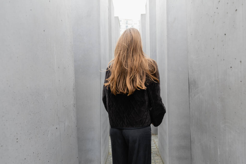 Вид ззаду на жінку в чорній куртці між каменями Меморіалу вбитих євреїв Європи - Фото, зображення