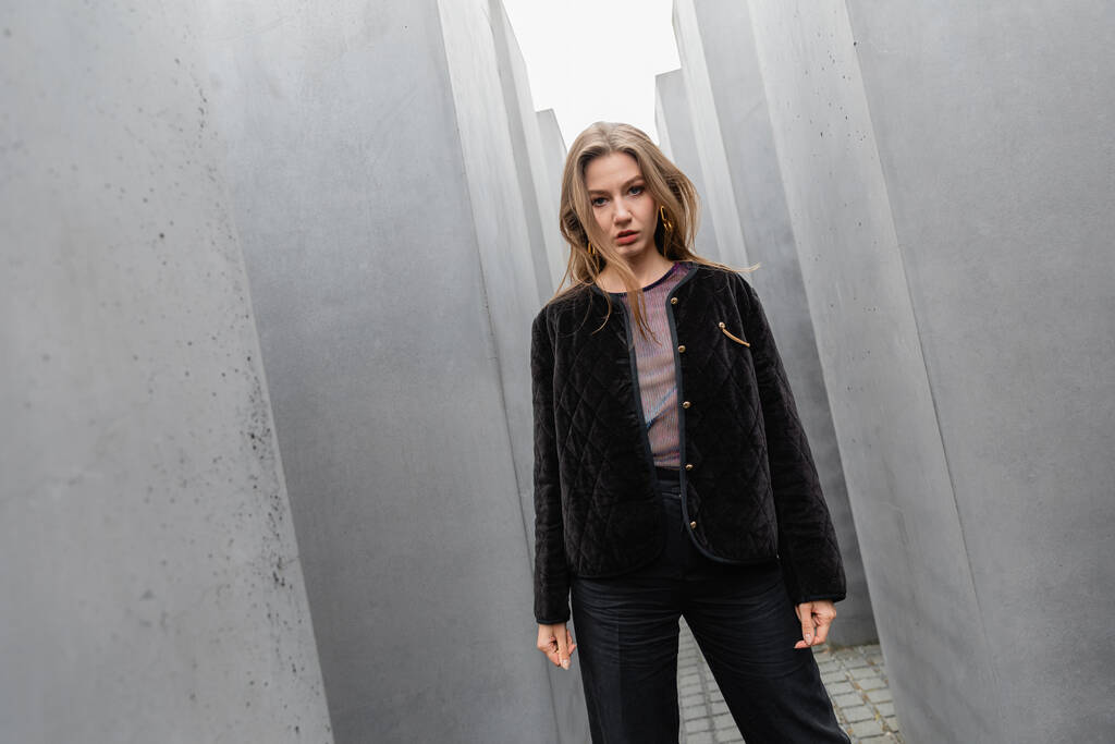 ベルリンでヨーロッパの殺害されたユダヤ人への記念碑の間に立っているジャケットのトレンディな若い女性  - 写真・画像