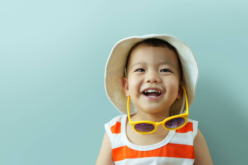 ポートレート青い隔離された背景で笑って帽子と黄色のサングラスを持つ愛らしいアジアの中国の小さな男の子。夏. - 写真・画像