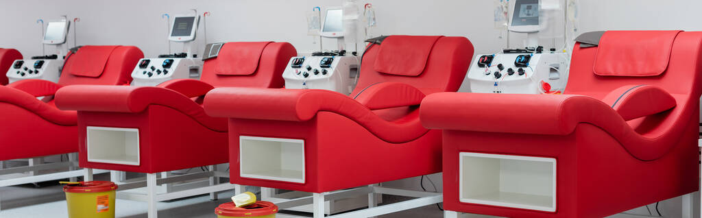 rij comfortabele medische stoelen met ergonomisch ontwerp, vuilnisemmers en geautomatiseerde transfusiemachines met monitoren in modern bloeddonatiecentrum, banner - Foto, afbeelding