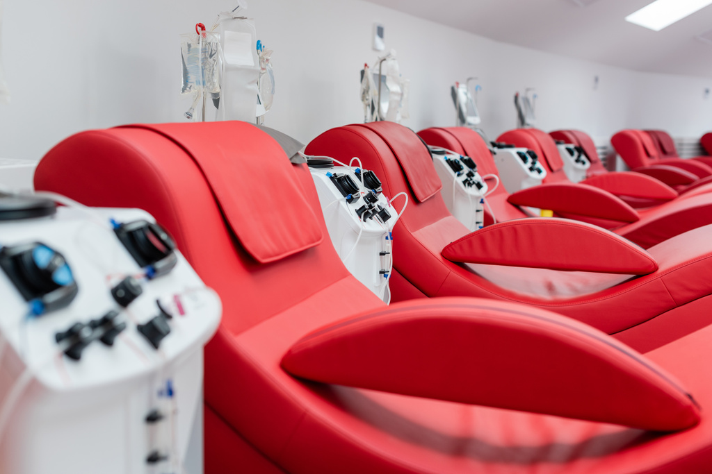 ряд удобных и эргономичных медицинских стульев возле автоматизированных машин для переливания крови и капельниц с инфузионными пакетами в современной лаборатории центра донорства крови - Фото, изображение