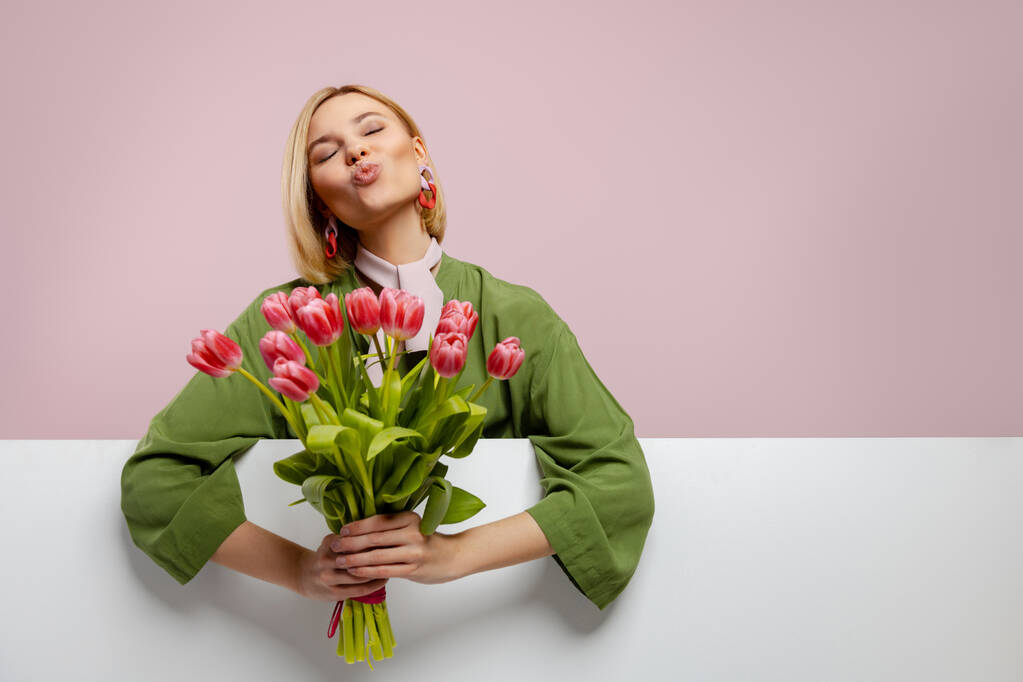 mooie jonge vrouw holding bos van tulpen en glimlachen tegen roze achtergrond - Foto, afbeelding
