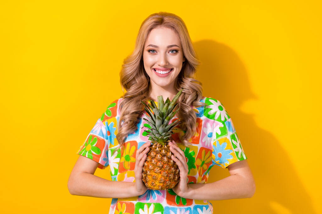 Portrét rozkošné zubaté zářící žena nosit květinový potisk tričko drží ananas obě ruce izolované na žlutém pozadí. - Fotografie, Obrázek