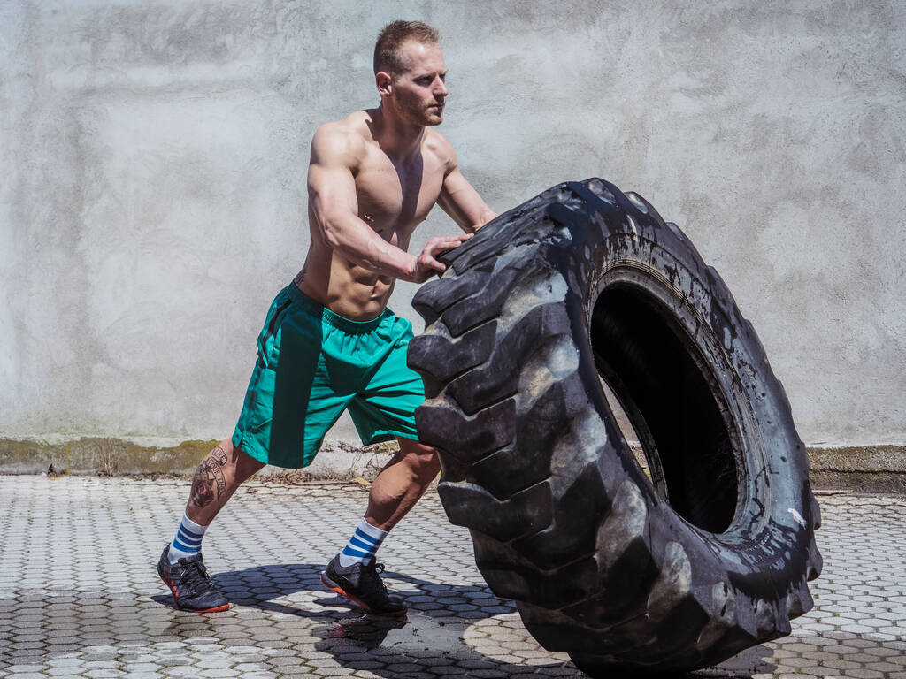 Handsome muscular young man exercising, flipping big truck tire outdoor - Photo, Image