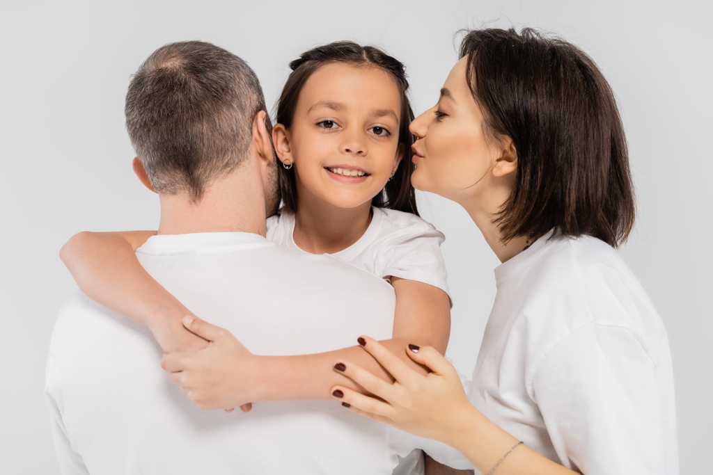 白いTシャツに身を包みながら夫の近くにいる10代の娘の頬にタトゥーと短い髪のキスを持つ母親,国際子どもの保護のための日,  - 写真・画像