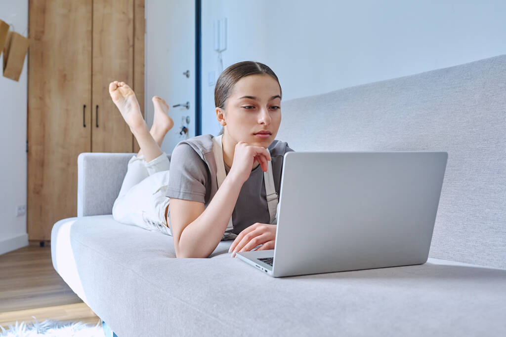 Chica adolescente en casa acostada en el sofá usando el ordenador portátil. Tecnología para el aprendizaje de la comunicación de ocio, estilo de vida moderno, concepto de adolescencia - Foto, imagen