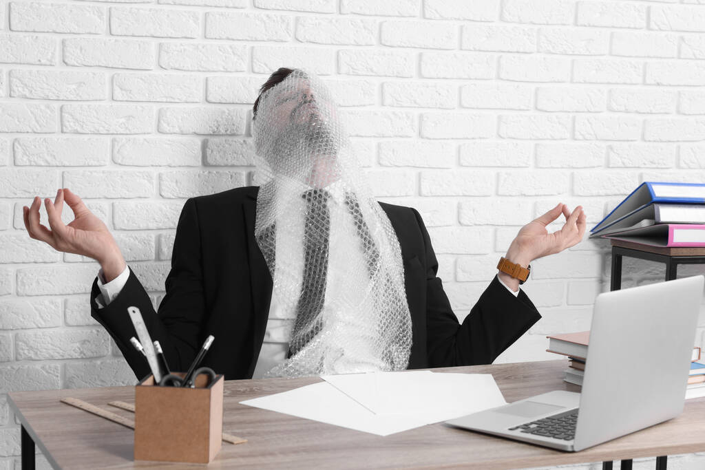 Бизнесмен медитирует с пузырьковой пленкой на лице на рабочем месте - Фото, изображение