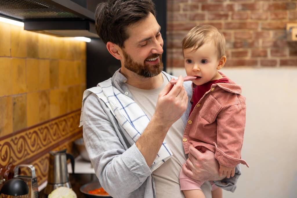 Junger Vater füttert kleine Tochter in Küche zu Hause. - Foto, Bild