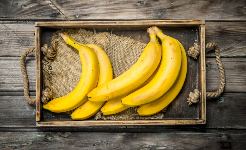 古いドレッシングの袋に新鮮なバナナ。黒い木製の背景に. - 写真・画像