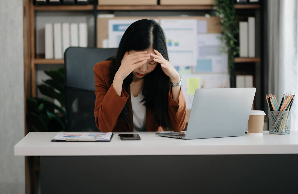 Азійська жінка відчуває, що мігрень голова напружена. Перевантажена бізнесменка фінансистка з ноутбуком в сучасному офісі.. - Фото, зображення
