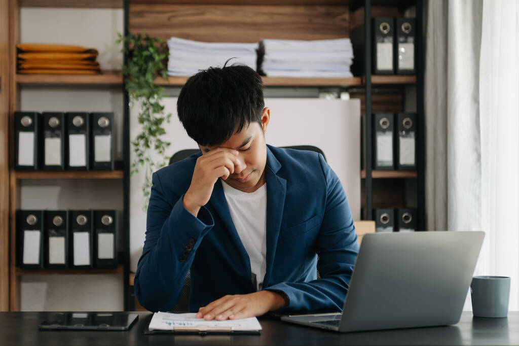 Frustré jeune homme d'affaires travaillant sur un ordinateur portable assis à son lieu de travail dans un bureau moderne - Photo, image