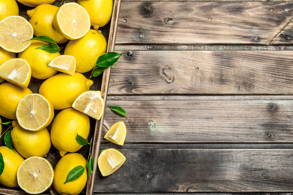 Juicy lemons with leaves in tray. On wooden background - Photo, Image