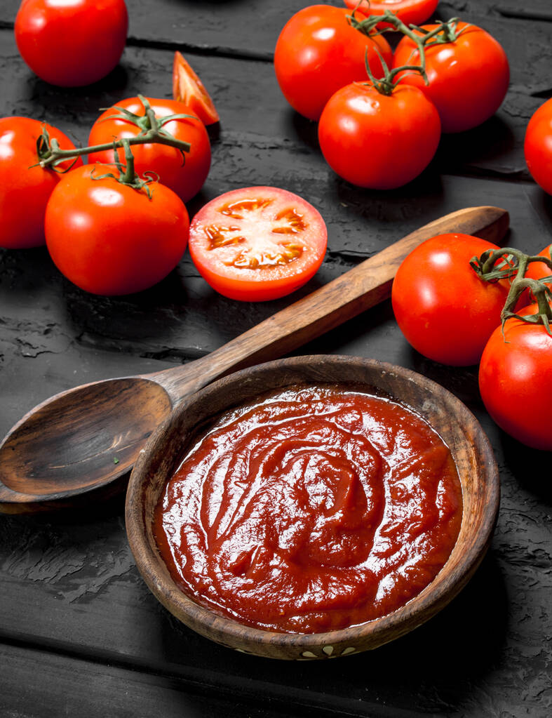 Molho de tomate em tigela com colher e tomates maduros. No fundo rústico preto
 - Foto, Imagem