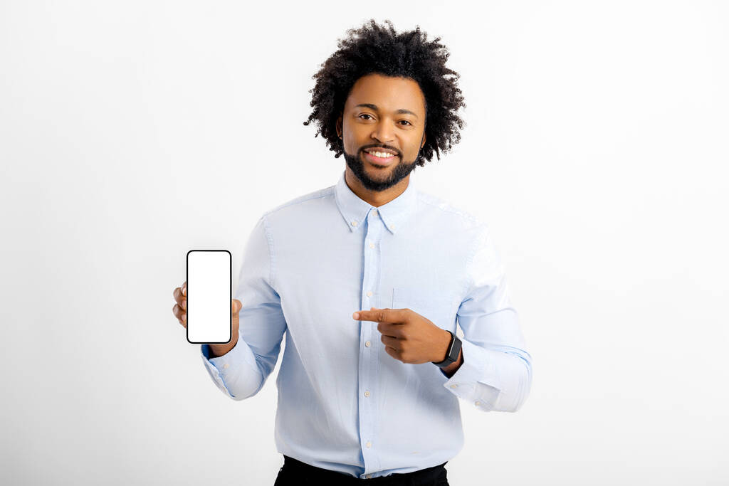 Beyaz gömlekli, beyaz tişörtlü, beyaz ekranlı akıllı telefonlu kıvırcık Afrikalı Amerikalı adam beyaz arka planda tek başına duruyor, erkek ofis çalışanı telefonu tutuyor ve yeni mobil uygulama tanıtımını yapıyor. - Fotoğraf, Görsel