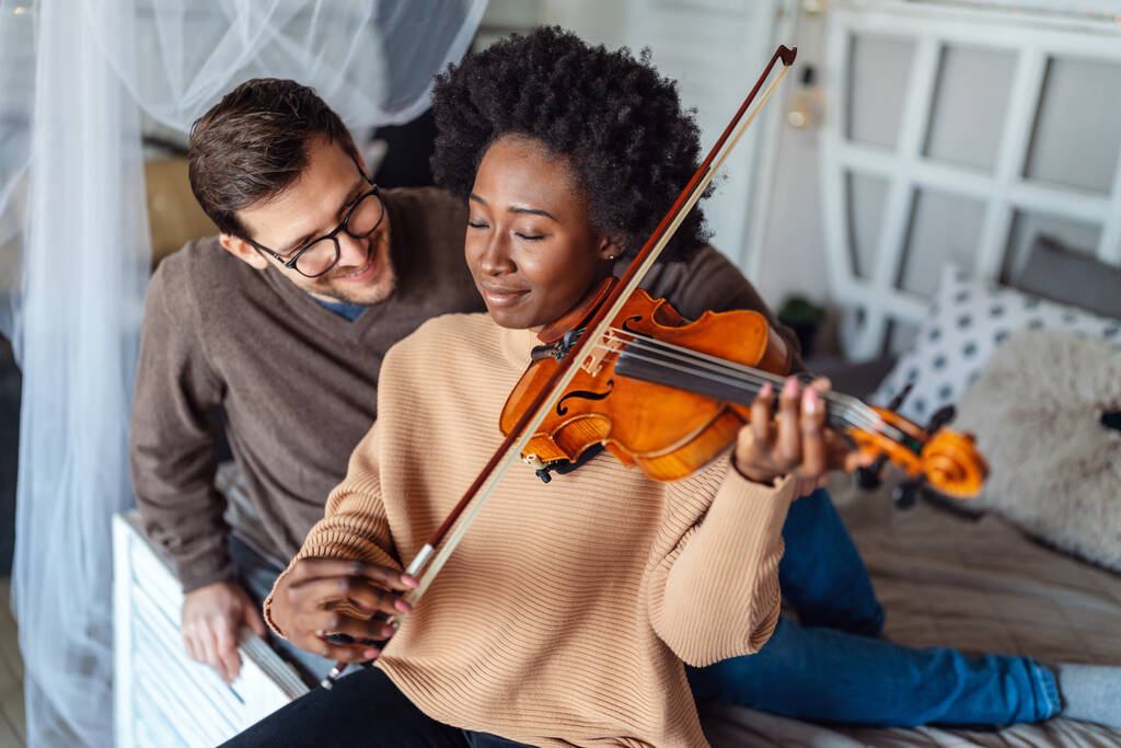 Young male private music teacher giving violin lessons to a woman at home. Couple love romance concept. - Photo, Image