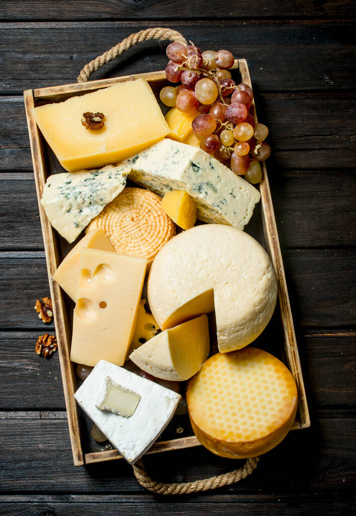 Different types of cheese in a wooden tray with grapes . On a wooden background. - Photo, Image