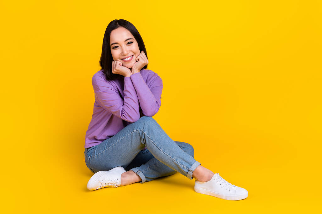 Полноразмерная фотография девушки с хорошим настроением боб прическа одета фиолетовая рубашка джинсы брюки сидя руки на чики изолированы на желтом цвете фоне. - Фото, изображение