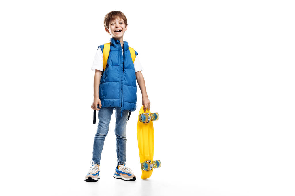 Pleine photo longue de rire petit garçon tenant skateboard jaune sur fond blanc. Retour à l'école - Photo, image
