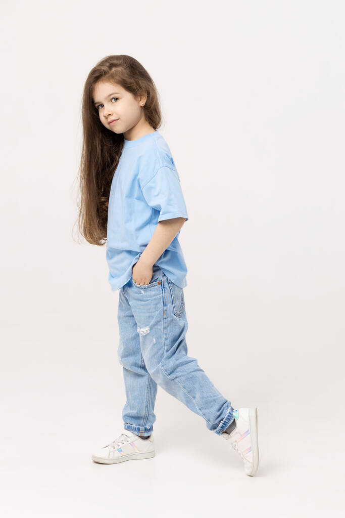 Portrait complet d'une enfant fille positive péchant un T-shirt bleu et un jean bleu isolé sur fond blanc.  - Photo, image