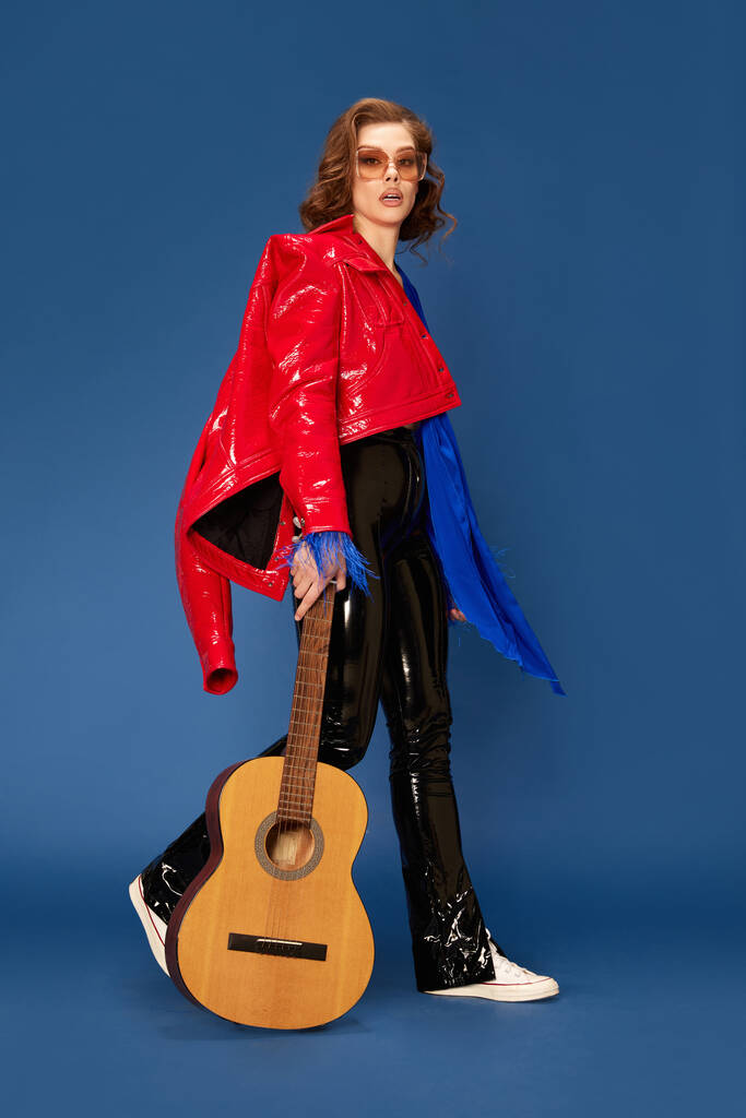 Retrato completo de menina bonita em roupas elegantes andando com guitarra contra fundo estúdio azul. Festival de música. Conceito de emoções humanas, moda feminina, beleza, festa, estilo de vida - Foto, Imagem