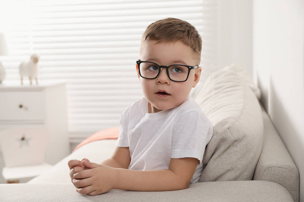 Aranyos kisfiú szemüvegben otthon a kanapén. - Fotó, kép