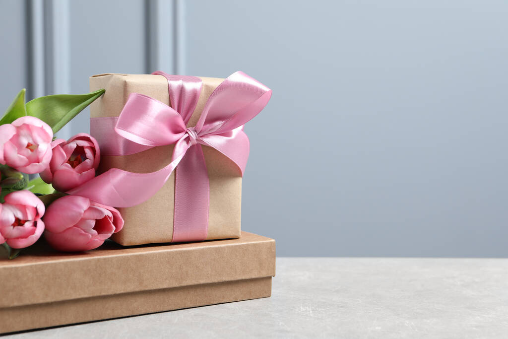 Kaunis lahjapaketti keula ja vaaleanpunainen tulppaani kukkia valopöydällä, tilaa tekstiä - Valokuva, kuva