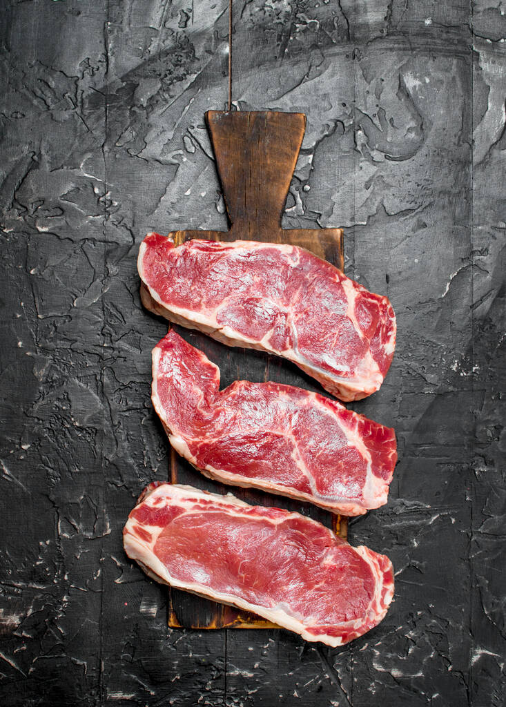 Raw beef steaks on cutting Board. On a black rustic background. - Photo, Image
