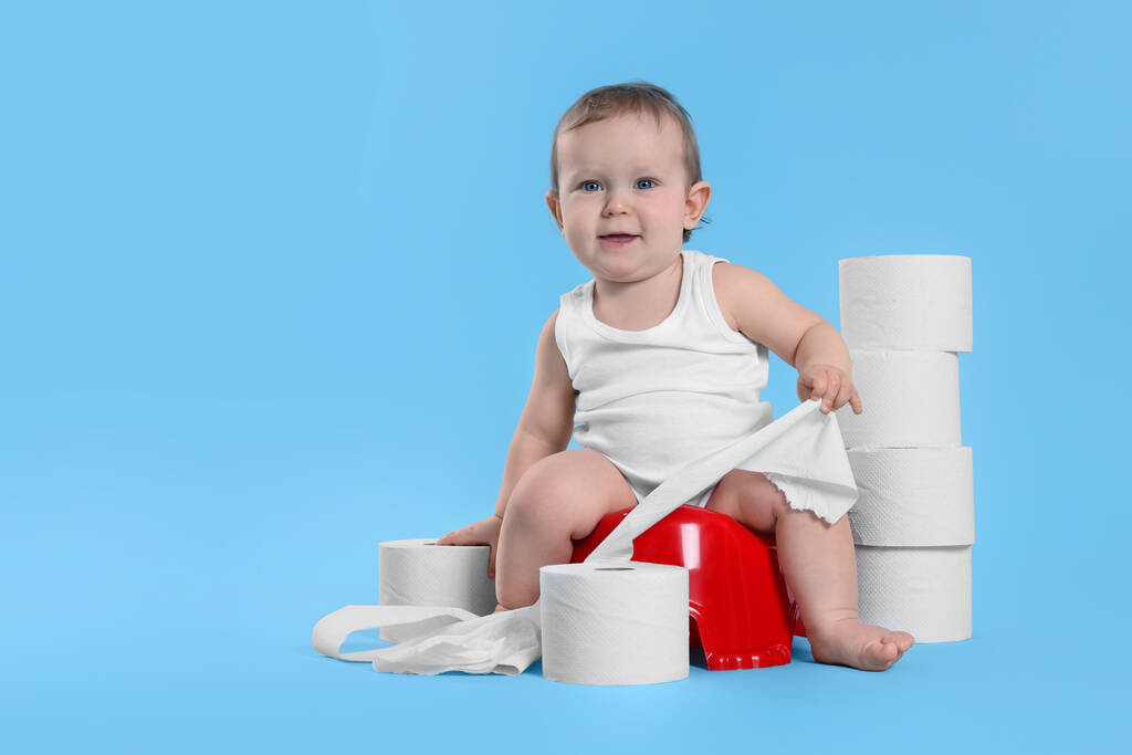 Маленький ребенок сидит на маленьком горшочке и стопке туалетной бумаги роллы на светло-голубом фоне. Пространство для текста - Фото, изображение