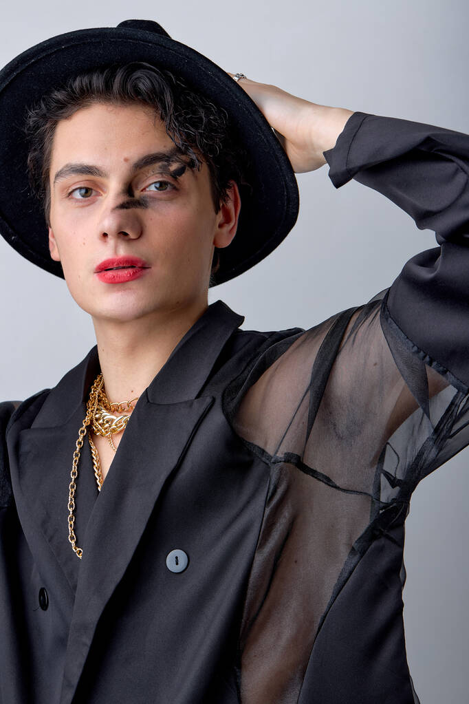 atraente jovem transexual homem LGBTQ sendo como mulher posando com corrente, no chapéu, lindo caucasiano cara mostrando auto-confiança, com batom vermelho e make-up isolado no fundo branco. - Foto, Imagem