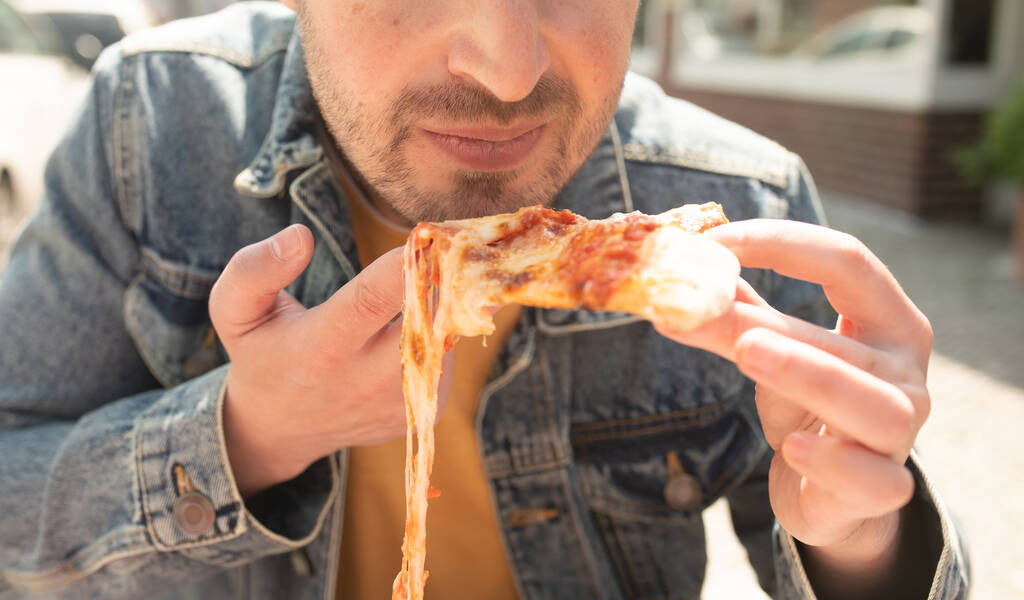 Hezký mladý muž jí kousek pizzy venku na ulici.        - Fotografie, Obrázek