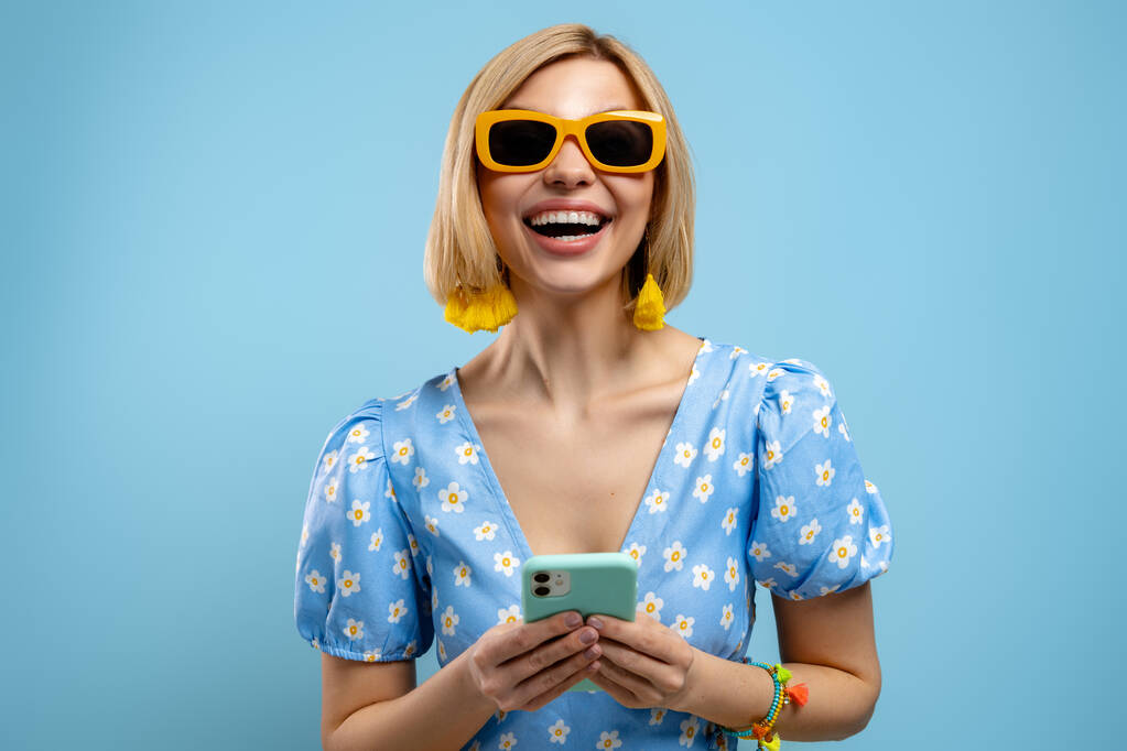 Возбужденная молодая женщина держит смартфон и улыбается на синем фоне - Фото, изображение