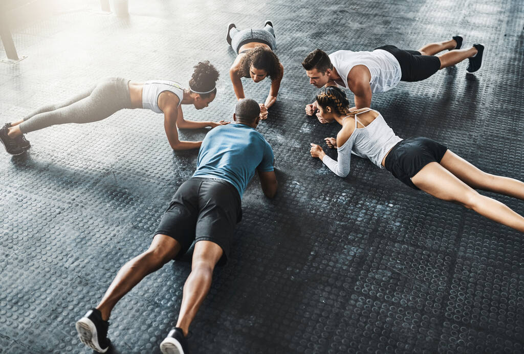The comfort zone has no place in a gym. a group of young people doing planks together during their workout in a gym - Photo, Image