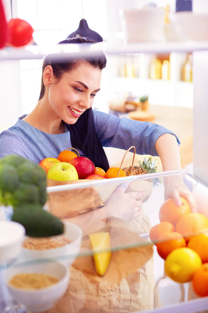 Hymyilevä nainen ottaa tuoreita hedelmiä jääkaapista, terveellistä ruokaa käsite. - Valokuva, kuva