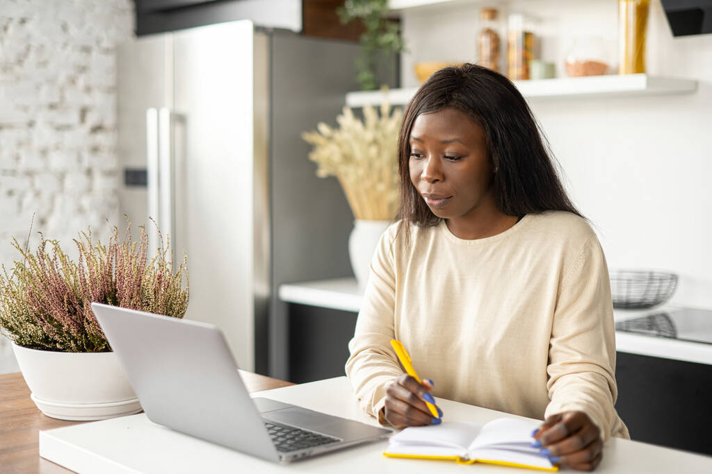 Egy gyönyörű fekete nő okos alkalmi viselet használ laptop számítógép egy modern otthoni irodában, női alkalmazott ír tervező, diák tanul a távolból, nézi webinar - Fotó, kép